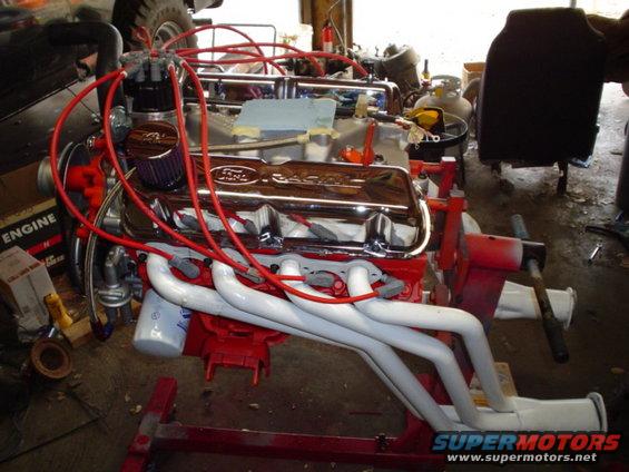 Ford V8 engine with chrome valve covers and red spark plug wires on an engine stand