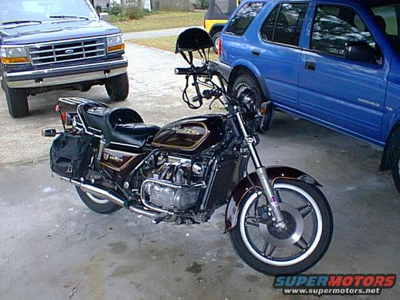 1981 Honda GL1100 Gold Wing motorcycle parked next to a blue SUV and a blue Ford truck