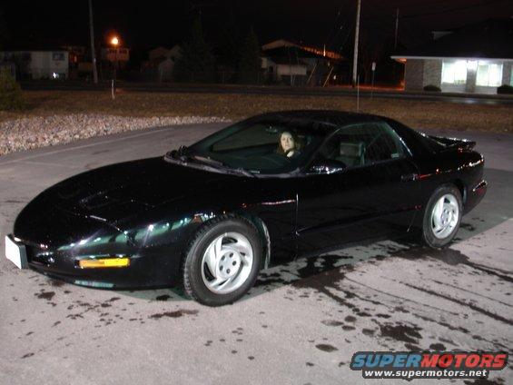 black Pontiac Firebird parked at night, woman in driver's seat