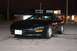 1981 Ford Mustang - A black coupe is parked outside a building at night, with its headlights on.