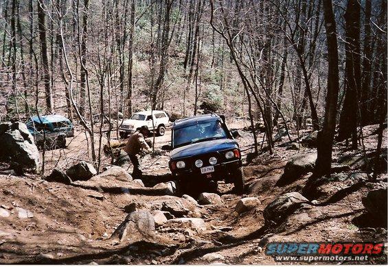 Dark blue SUV navigates rocky terrain with two other SUVs behind it