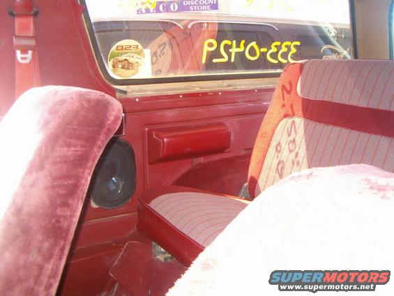 Interior view of a 1985 Ford Bronco showing red velour seats and door panel, with a sticker on the rear window