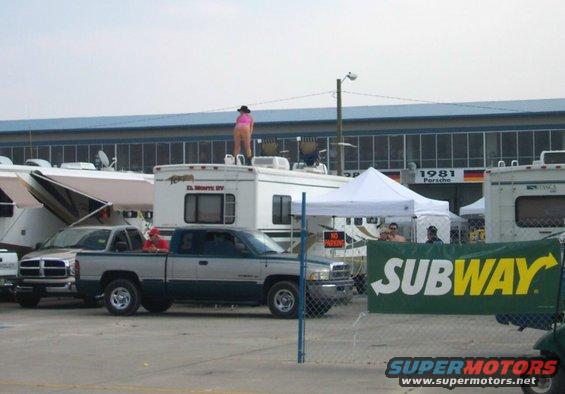 Two-tone pickup truck parked next to RVs, with a person on top of an RV