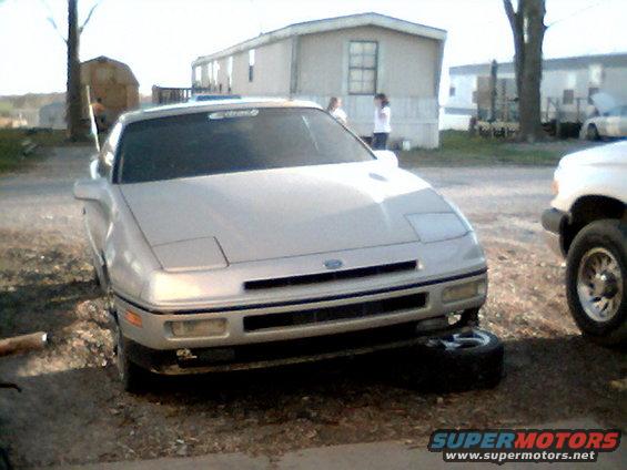 Silver 1989 Ford Probe with a flat tire, parked in front of mobile homes