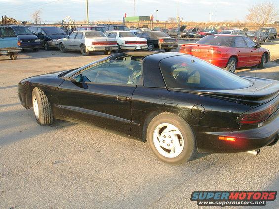 Black sports car with a t-top roof and white five-spoke wheels, parked on asphalt