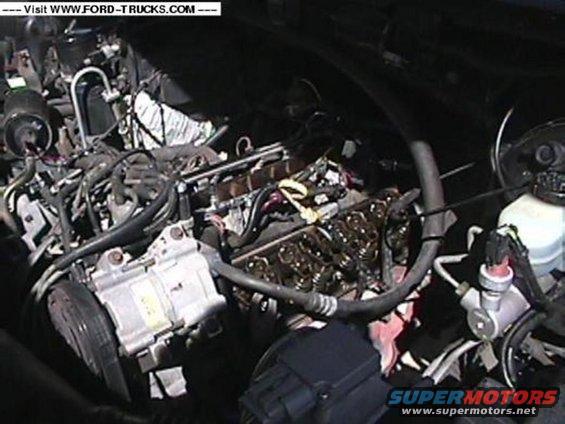 Engine bay with visible engine components, hoses, and wiring. Text overlay reads 'Visit WWW.FORD-TRUCKS.COM'
