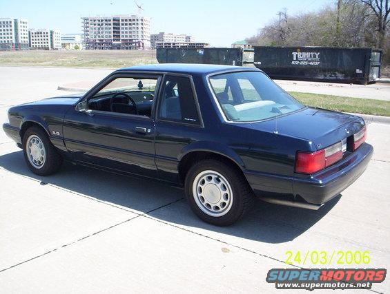 1991 Ford Mustang coupe parked on pavement, side view. Buildings and dumpsters in background