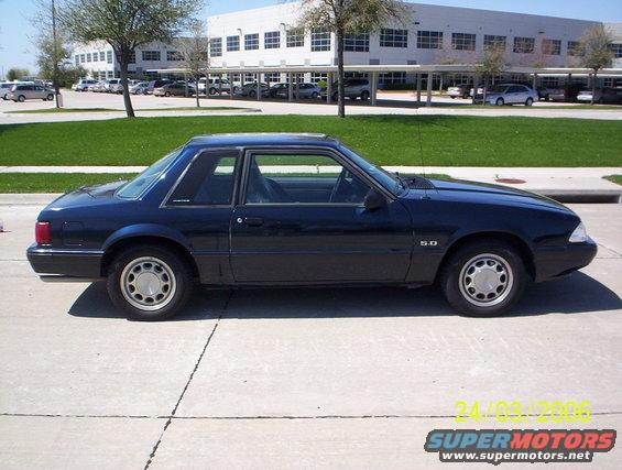 Dark blue 1991 Ford Mustang coupe parked on concrete, side view. "5.0" badge visible on fender