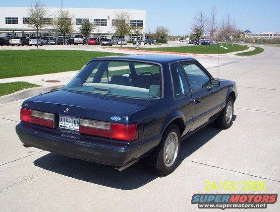 dark blue coupe parked on pavement, building and trees in background
