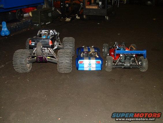 three remote control vehicles lined up: a black monster truck, a blue and white striped car, and a red buggy