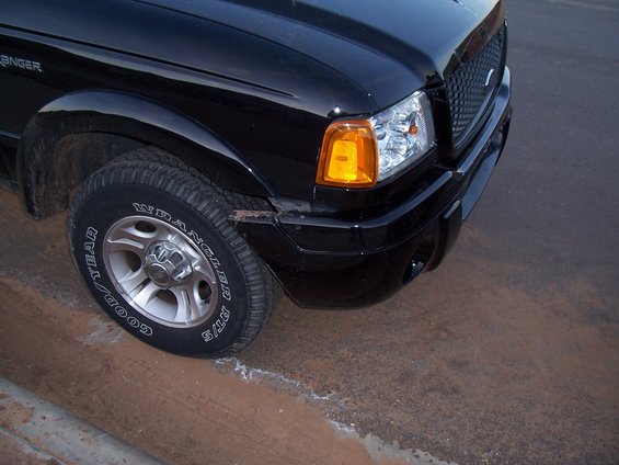 Black 2003 Ford Ranger truck front corner, tire on dirt curb, minor bumper damage