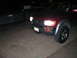 1996 Toyota 4Runner - Front corner view of a red 1996 Toyota 4Runner, parked next to a dark pickup truck at night.