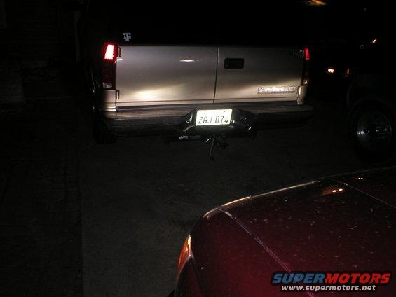 Rear of a silver Chevrolet van with a license plate reading 2GJ 074. A red car is in the foreground