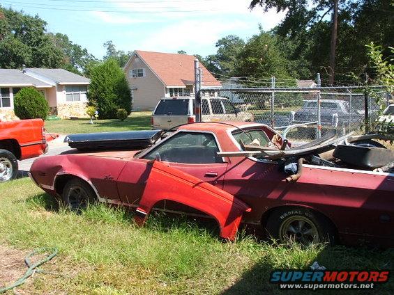 Red 1972 Ford Ranchero with detached fender, parked in overgrown grass