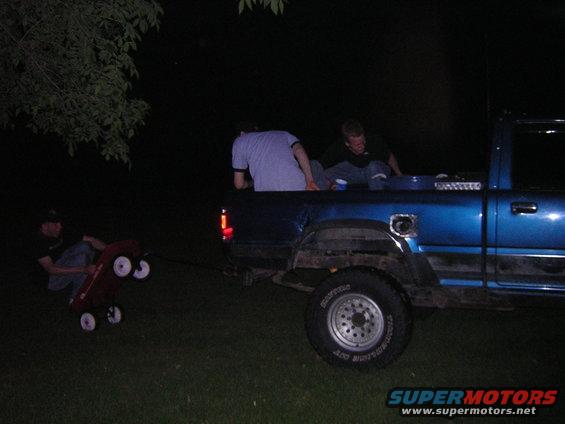 Blue pickup truck bed with people, red wagon being pulled at night