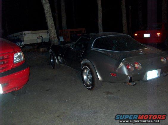 Gray 1979 Chevrolet Corvette, rear 3/4 view, parked at night next to a red truck and a trailer