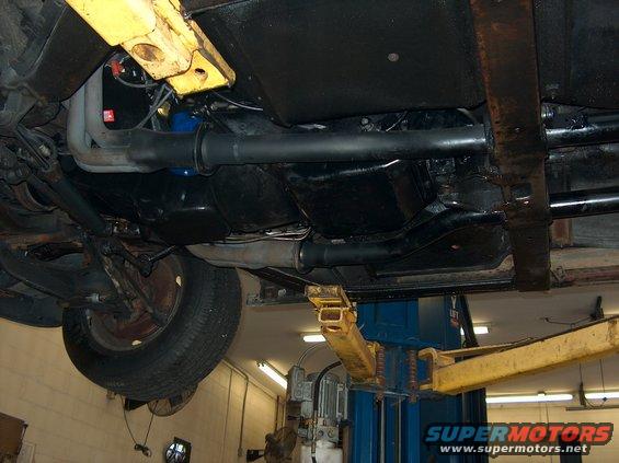 Underside view of a car on a lift, showing exhaust and drive shaft