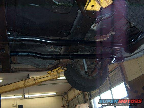 Undercarriage of a vehicle on a lift, showing exhaust pipes and a rear tire