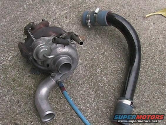 Turbocharger and a black intake pipe with blue and gray connectors, lying on a concrete surface