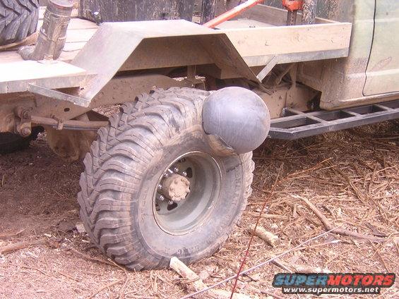 Close-up of a large, knobby off-road tire on a vehicle, with a gray spherical object attached to the side of the tire