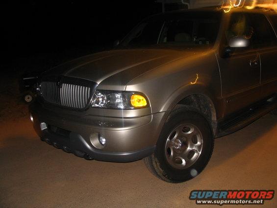 Front corner of a gold Lincoln Navigator SUV, showing grille, headlights, and wheel