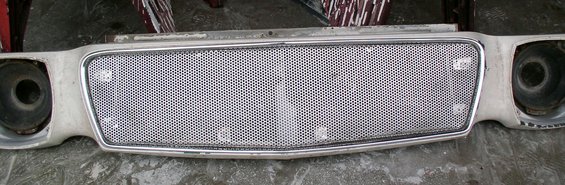 Car grille with a honeycomb pattern and chrome trim, showing headlight openings on either side