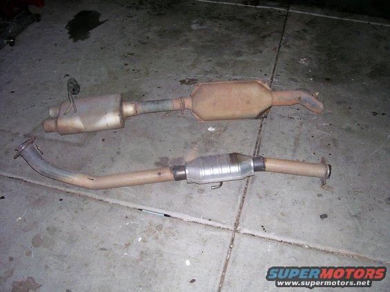 two exhaust pipes with mufflers and catalytic converters laid out on concrete floor