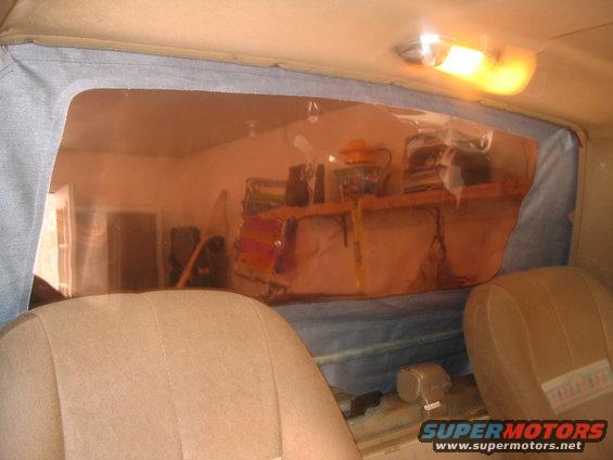 Interior of a vehicle with tan seats and a clear plastic rear window showing a cluttered shelf