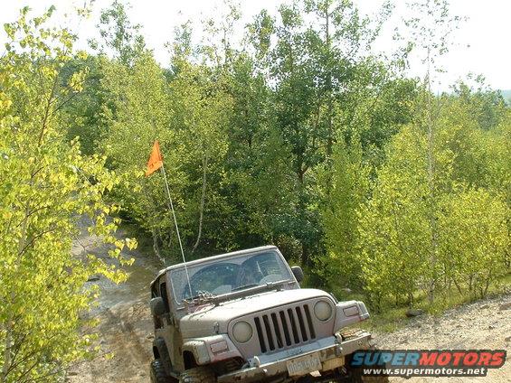 Tan Jeep Wrangler on a dirt trail with an orange flag