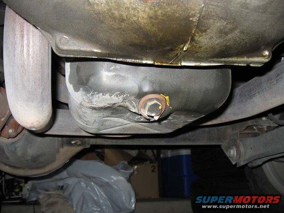 underside view of a vehicle's oil pan with a drain plug and exhaust pipe visible
