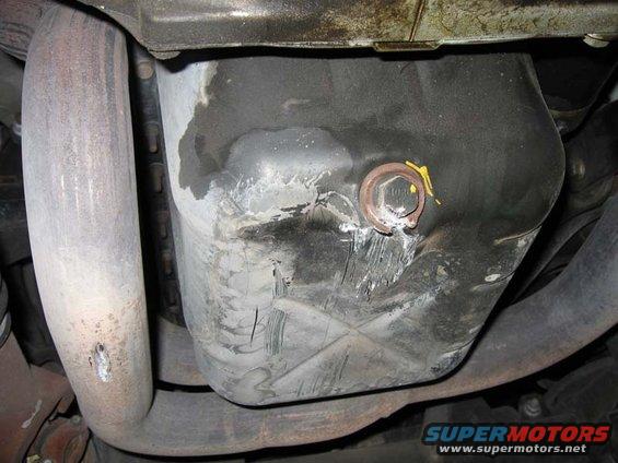 Underside view of a vehicle's oil pan and exhaust pipe, showing some wear and a drain plug