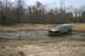 1989 Ford Bronco - A Jeep Cherokee XJ navigates a challenging muddy terrain, kicking up water and dirt.
