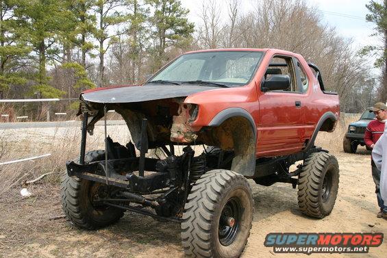 Orange modified off-road vehicle with missing front end and large tires, parked outdoors