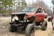 1989 Ford Bronco - A heavily modified orange off-road vehicle sits in a dirt lot with another vehicle in the background.