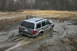 1989 Ford Bronco - A silver SUV is deeply stuck in thick mud, with its rear end partially submerged.