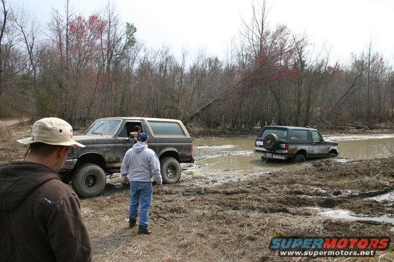 Muddy brown 1987 Ford Bronco stuck in a muddy puddle with another Bronco behind it