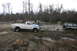 1989 Ford Bronco - Two trucks are in a muddy, wooded area. One is driving on a dirt path, while the other is stuck in the mud.