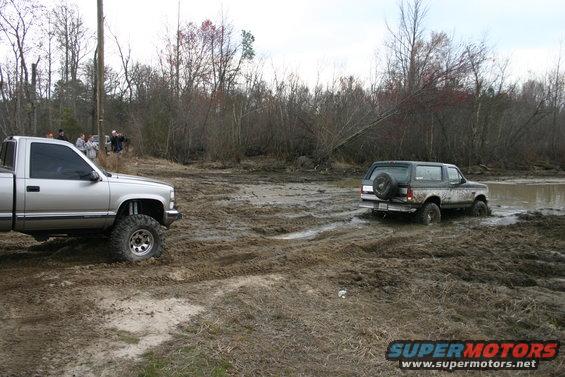 Dark green Ford Bronco stuck in mud, spare tire on rear door, seen from rear