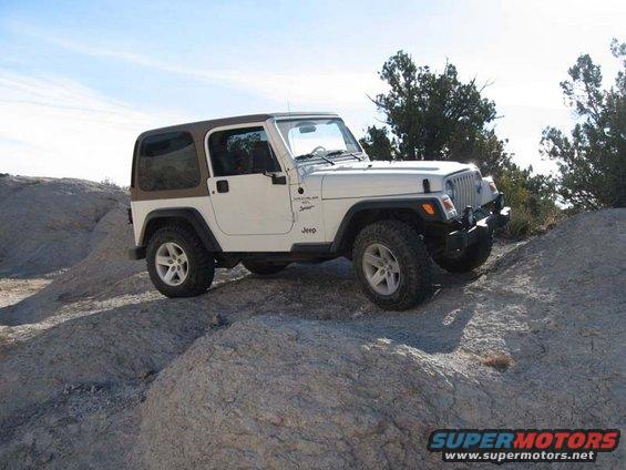 White Jeep Wrangler with brown hardtop on rocky terrain, front-right quarter view