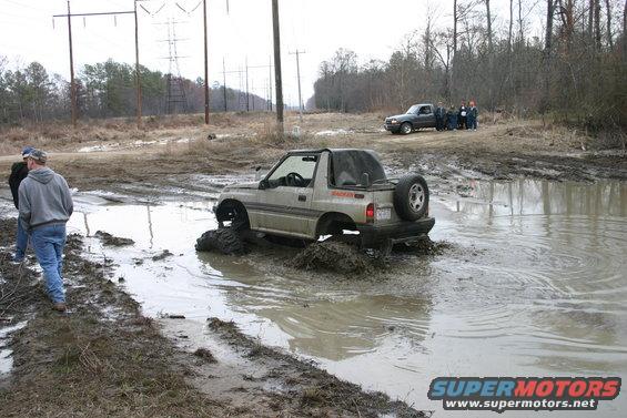 Suzuki Samurai stuck in deep mud with people watching and a pickup truck in the background