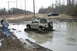 1989 Ford Bronco - A Suzuki Samurai navigates a challenging muddy terrain, while a pickup truck and onlookers observe the off-road adventure.