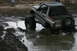 1989 Ford Bronco - An off-road vehicle navigates through a muddy terrain, with one wheel deep in the mire.