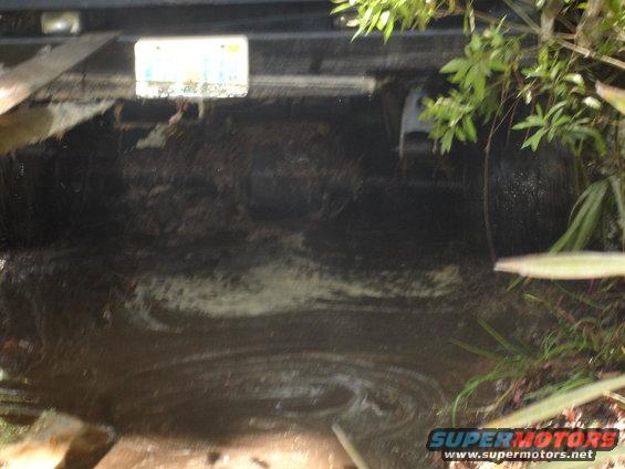 Vehicle stuck in muddy water, showing undercarriage and tires