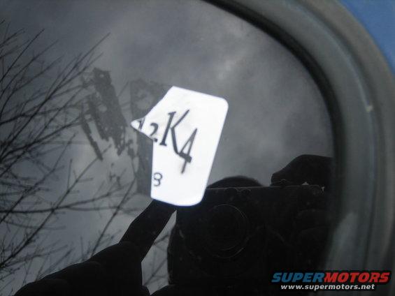 Close-up of a sticker with '2K4' and '3' on a car window, reflecting trees and a camera
