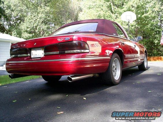 Red convertible sedan parked on driveway, rear view. Has dual exhaust pipes and aftermarket wheels