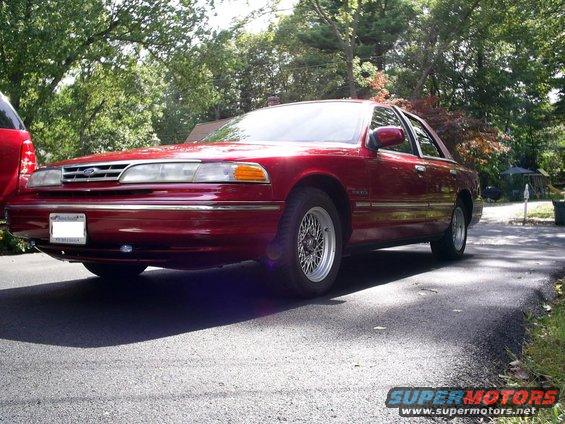 Red 1995 Ford Crown Victoria sedan with chrome trim and wire wheels, parked on asphalt