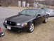 1995 Ford Crown Victoria - This black sedan features a distinctive black grille and chrome wheels, with other vehicles visible in the background.