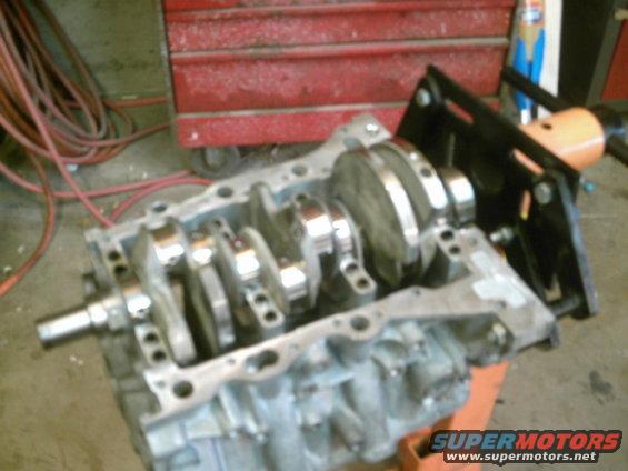 Engine block with crankshaft mounted on an engine stand. Red tool chest and red cables in background