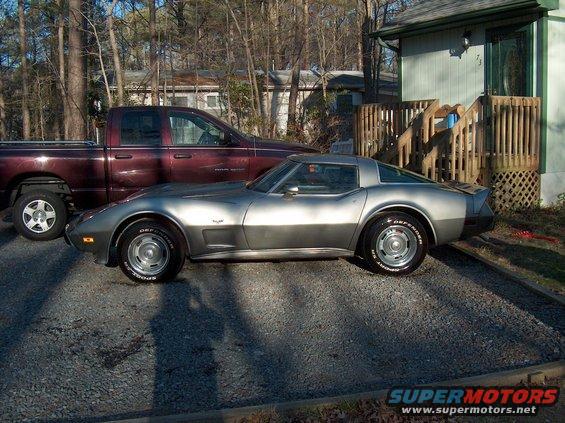 Side view of a silver 1979 Chevrolet Corvette parked next to a maroon pickup truck