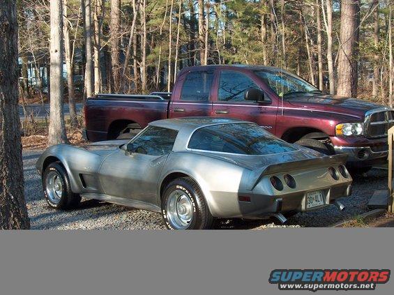 Silver 1979 Chevrolet Corvette with a spoiler and quad taillights, parked next to a maroon pickup truck